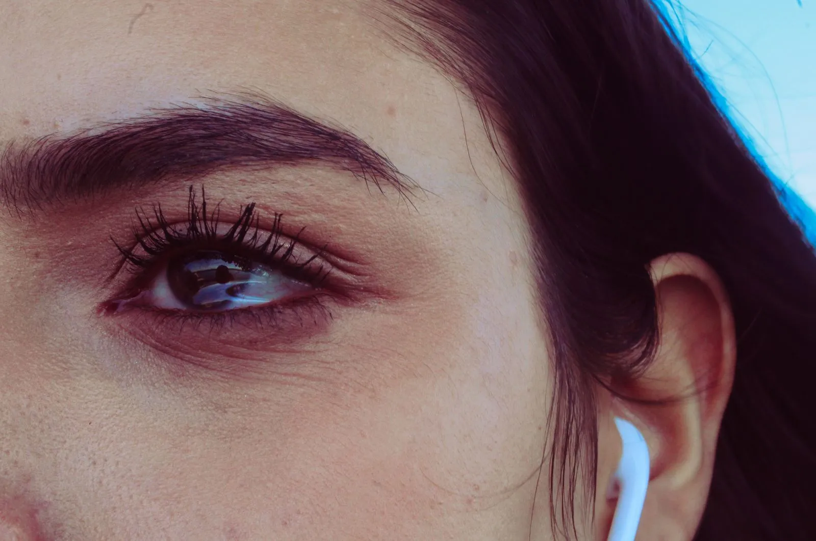 Detailed close-up of a woman's eye and ear with an earbud, capturing expression and texture.